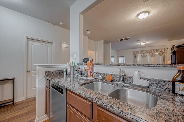 kitchen featuring visible vents, brown cabinetry, dishwasher, dark stone countertops, and a sink