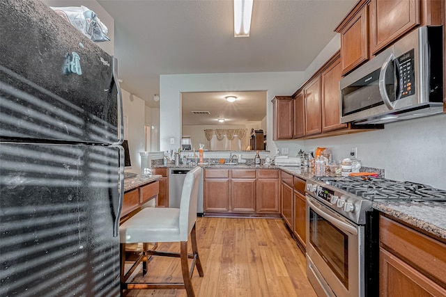 kitchen featuring stainless steel appliances, light wood finished floors, light stone countertops, and brown cabinets