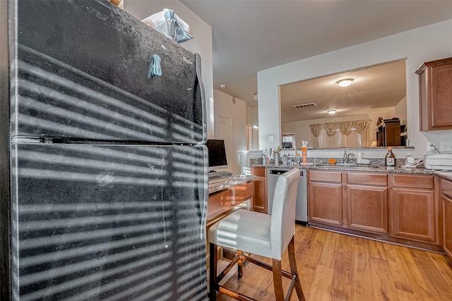 kitchen with visible vents, brown cabinetry, freestanding refrigerator, stone countertops, and light wood-style floors