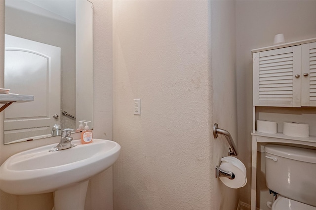 bathroom with a textured wall, a sink, and toilet