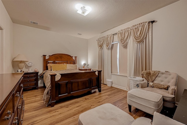 bedroom with light wood-style floors, visible vents, and a textured ceiling