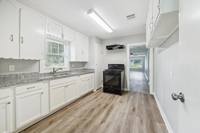 kitchen with light stone countertops, white cabinets, a sink, and gas stove