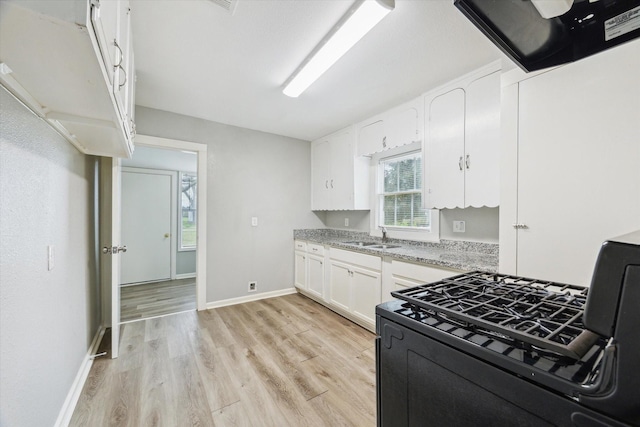 kitchen with baseboards, gas range, light wood-style floors, white cabinetry, and a sink