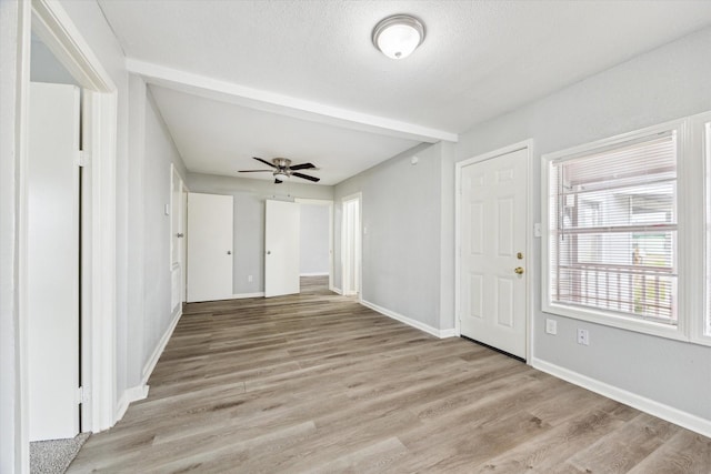 interior space with beam ceiling, light wood finished floors, a ceiling fan, a textured ceiling, and baseboards