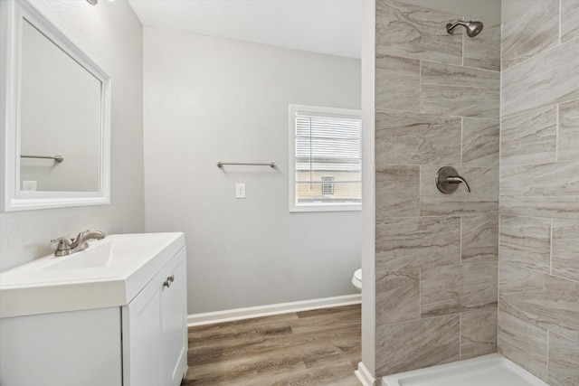 full bathroom featuring baseboards, toilet, wood finished floors, a tile shower, and vanity