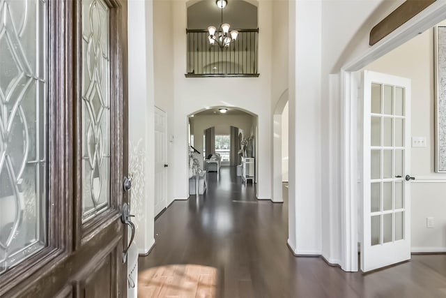 entrance foyer with baseboards, arched walkways, a towering ceiling, dark wood-style flooring, and a chandelier