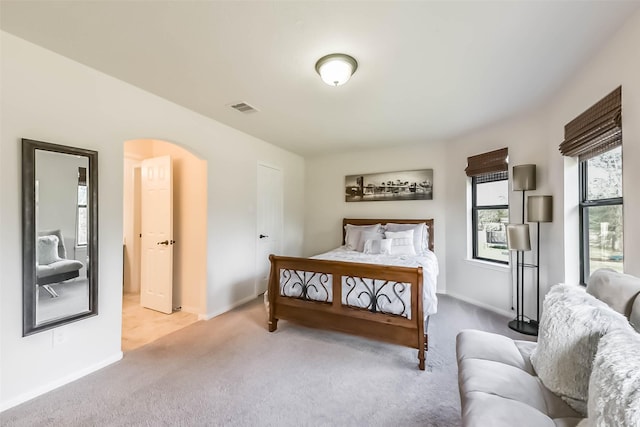 bedroom featuring arched walkways, baseboards, visible vents, and light colored carpet