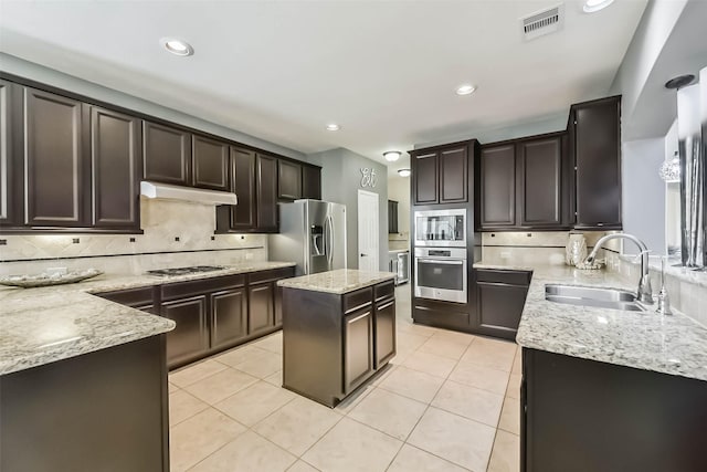 kitchen featuring light stone counters, a center island, stainless steel appliances, a sink, and under cabinet range hood