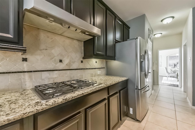 kitchen with stainless steel appliances, backsplash, light tile patterned flooring, light stone countertops, and wall chimney exhaust hood