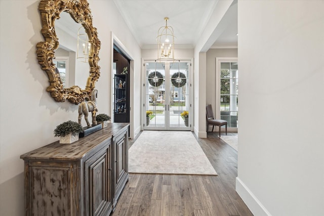 entrance foyer with ornamental molding, a notable chandelier, baseboards, and wood finished floors