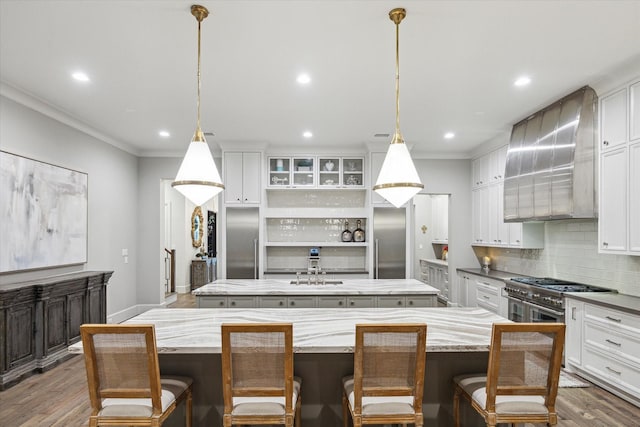 kitchen with wood finished floors, a kitchen island, high quality appliances, wall chimney range hood, and decorative backsplash