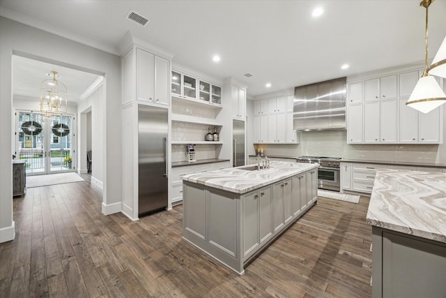 kitchen with visible vents, high quality appliances, wall chimney range hood, decorative backsplash, and dark wood-style floors