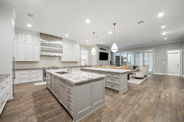 kitchen with a center island with sink, visible vents, high end stainless steel range, gray cabinets, and wall chimney range hood