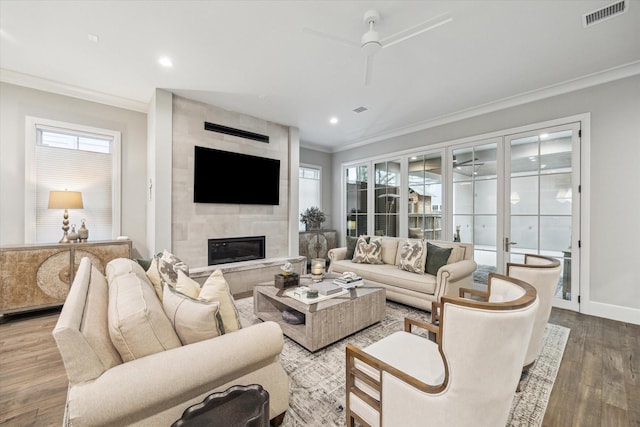 living room featuring baseboards, visible vents, wood finished floors, crown molding, and a fireplace