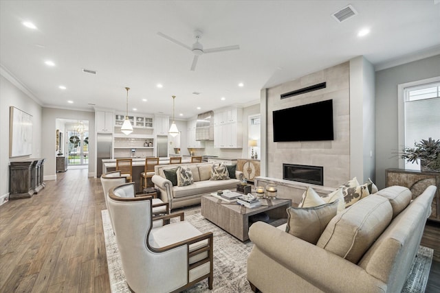 living room with recessed lighting, wood finished floors, visible vents, a tiled fireplace, and crown molding