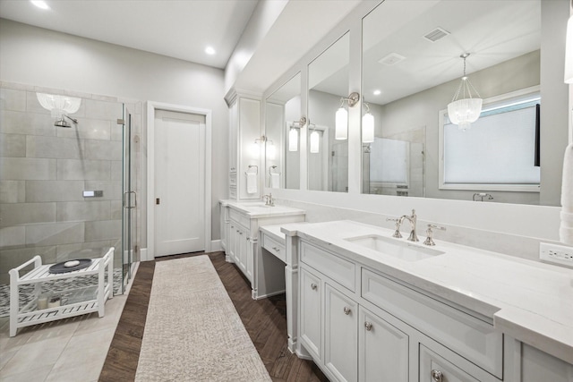 full bath featuring a stall shower, visible vents, two vanities, and a sink