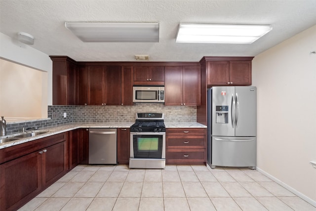 kitchen with light tile patterned floors, tasteful backsplash, appliances with stainless steel finishes, light stone countertops, and a sink