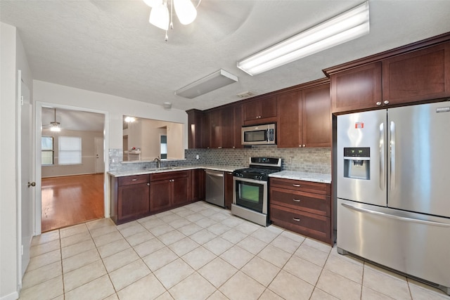 kitchen featuring tasteful backsplash, appliances with stainless steel finishes, light stone countertops, a sink, and light tile patterned flooring