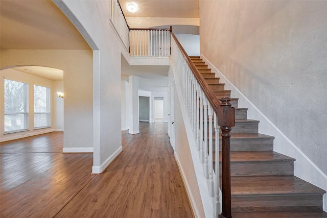 stairs featuring wood finished floors, arched walkways, a towering ceiling, and baseboards