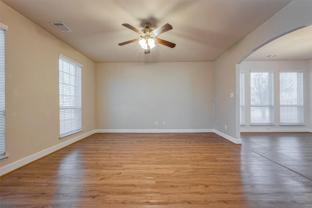 spare room featuring wood finished floors, visible vents, arched walkways, and a wealth of natural light