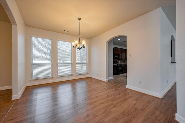 unfurnished dining area featuring visible vents, baseboards, an inviting chandelier, wood finished floors, and arched walkways