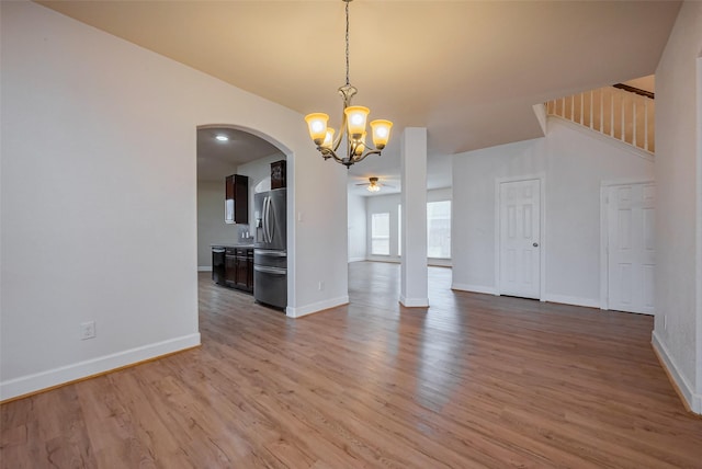 interior space with baseboards, light wood-style flooring, arched walkways, stairs, and ceiling fan with notable chandelier