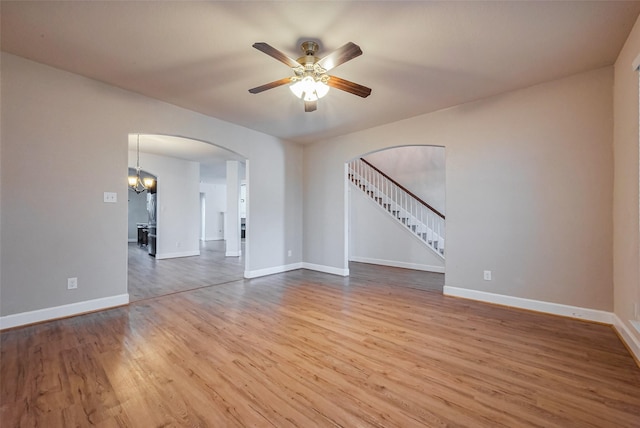 unfurnished room featuring a ceiling fan, wood finished floors, arched walkways, baseboards, and stairs