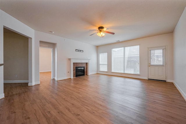 unfurnished living room featuring a ceiling fan, wood finished floors, baseboards, and a tile fireplace