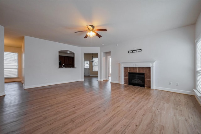 unfurnished living room featuring a tiled fireplace, wood finished floors, a ceiling fan, and baseboards