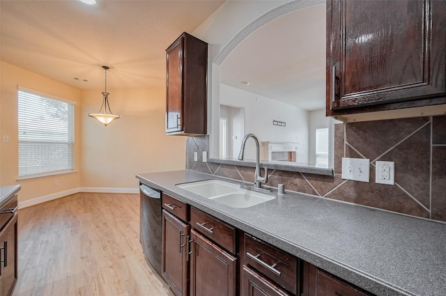 kitchen featuring a sink, tasteful backsplash, arched walkways, light wood finished floors, and dishwashing machine