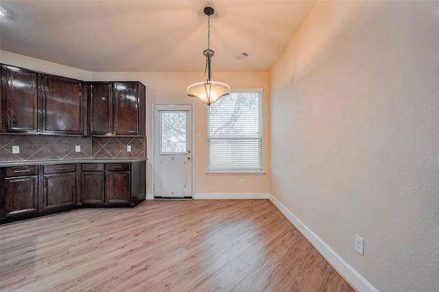 kitchen with tasteful backsplash, light wood-style floors, baseboards, dark brown cabinets, and hanging light fixtures