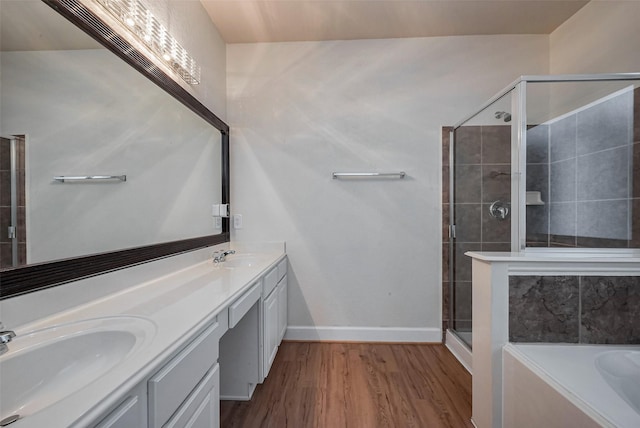 full bathroom featuring a shower stall, double vanity, wood finished floors, a bath, and a sink