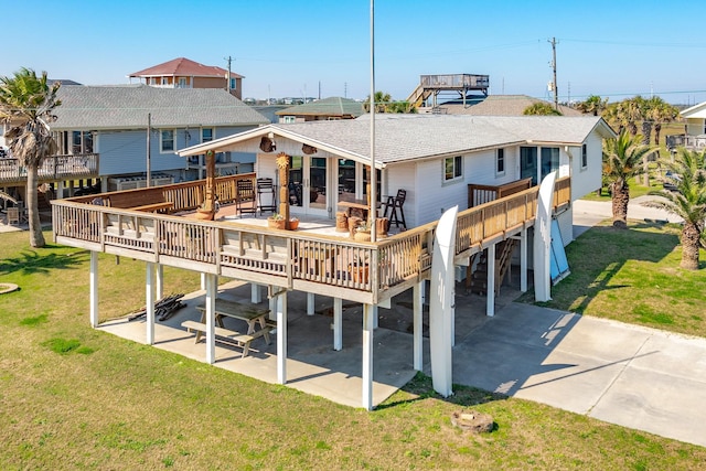 rear view of property with a deck, a patio, a lawn, roof with shingles, and a residential view