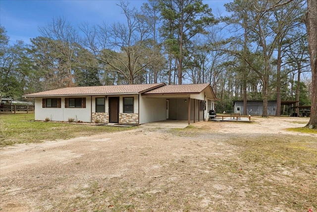 view of front of property with an attached carport, stone siding, dirt driveway, and a front yard