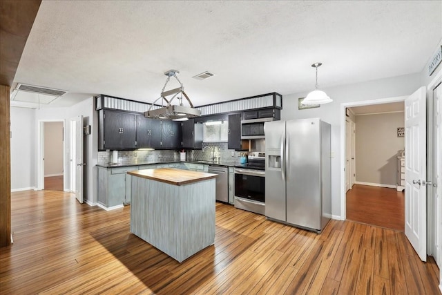 kitchen with a center island, decorative light fixtures, stainless steel appliances, butcher block counters, and visible vents