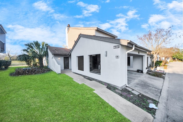 rear view of house with driveway, a lawn, a chimney, and stucco siding