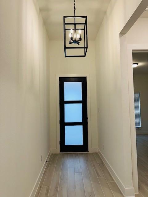 doorway featuring a chandelier, baseboards, and light wood finished floors