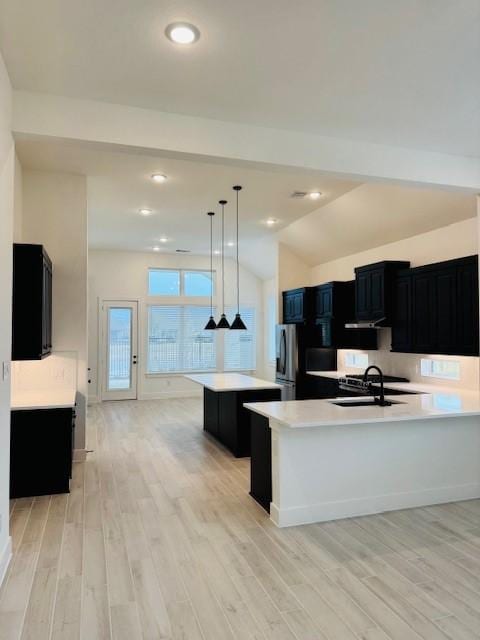 kitchen featuring pendant lighting, light countertops, a kitchen island with sink, and dark cabinets