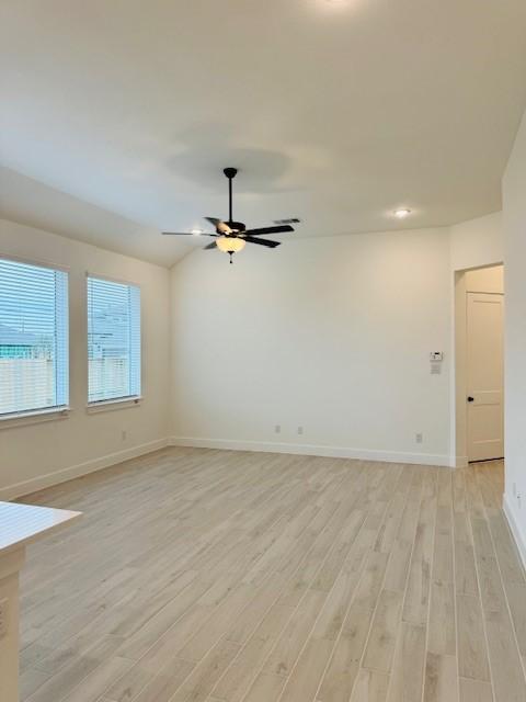 spare room featuring light wood finished floors, ceiling fan, baseboards, and vaulted ceiling