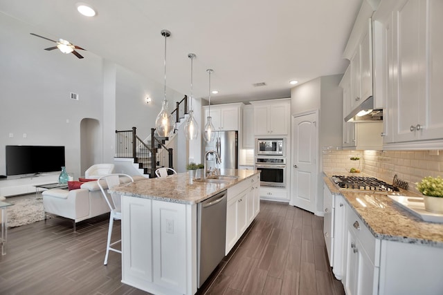 kitchen with a center island with sink, stainless steel appliances, open floor plan, white cabinets, and a sink