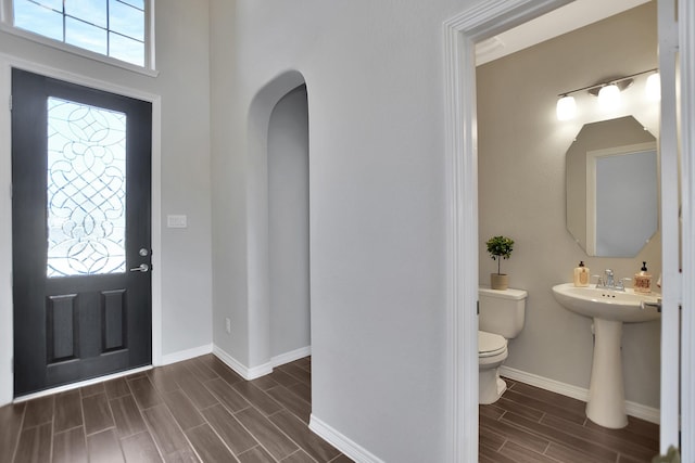 foyer with arched walkways, wood finish floors, plenty of natural light, and baseboards