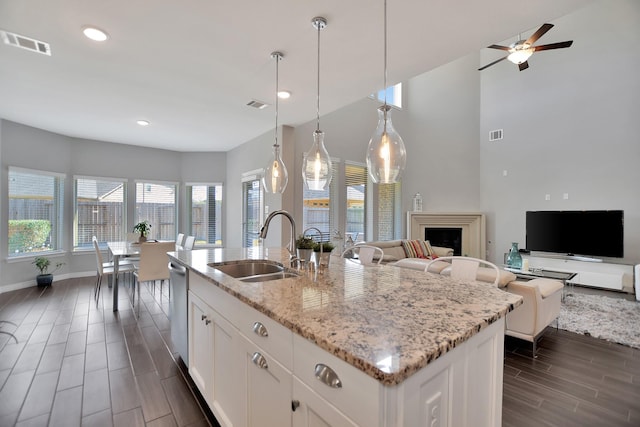 kitchen with visible vents, an island with sink, light stone counters, hanging light fixtures, and white cabinetry