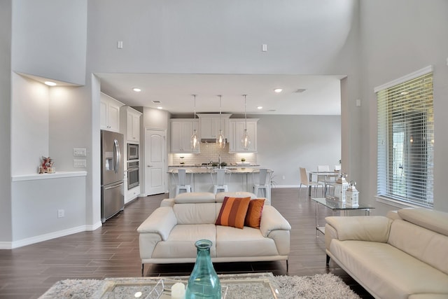 living room with a towering ceiling, visible vents, baseboards, and dark wood finished floors