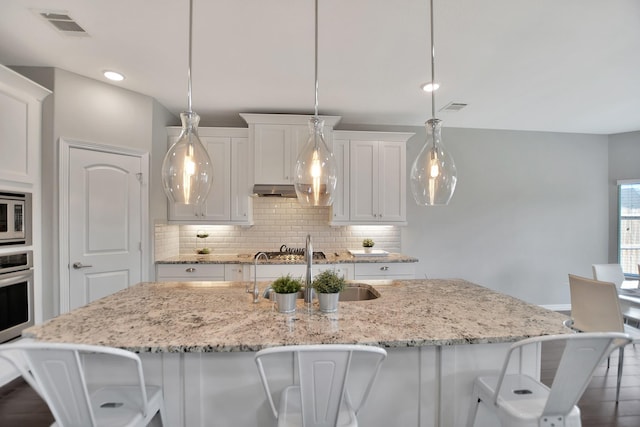 kitchen with stainless steel appliances, visible vents, white cabinetry, a center island with sink, and pendant lighting