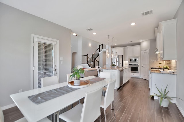 dining area featuring visible vents, stairs, arched walkways, and dark wood finished floors