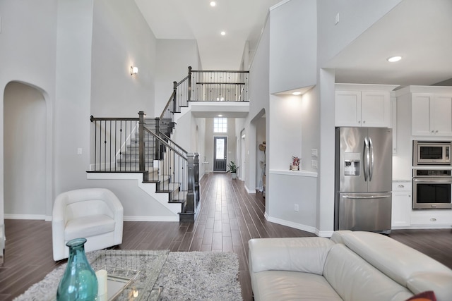 living area featuring arched walkways, stairway, a high ceiling, dark wood-type flooring, and baseboards