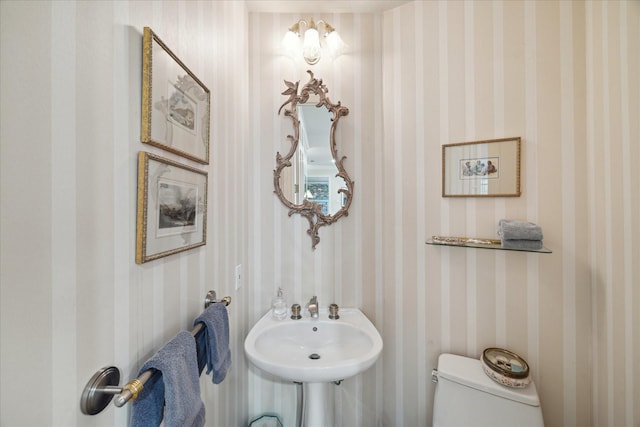 half bathroom featuring a sink, toilet, and wallpapered walls