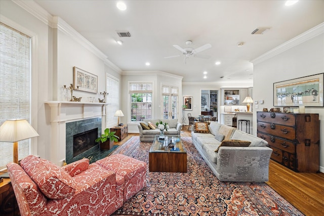 living area featuring ornamental molding, a high end fireplace, visible vents, and wood finished floors