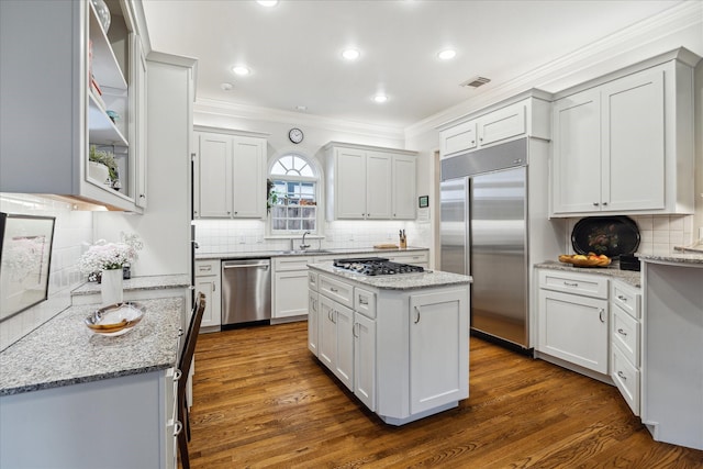 kitchen featuring stainless steel appliances, white cabinets, a kitchen island, a sink, and light stone countertops