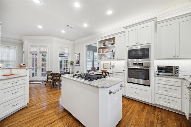 kitchen featuring light stone counters, a toaster, stainless steel gas cooktop, white cabinetry, and a center island